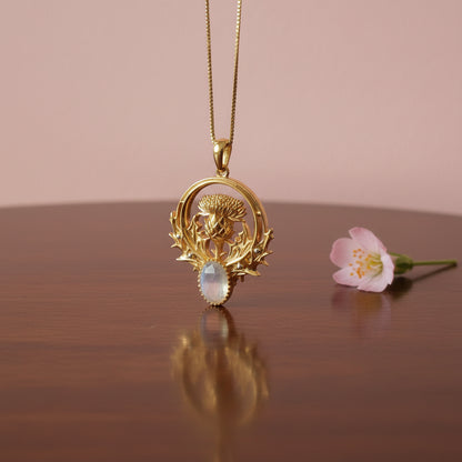 Gold pendant with thistle design and moonstone on a gray fabric background